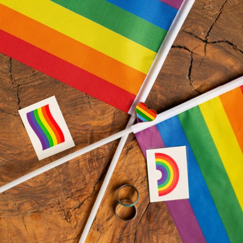 Rainbow pride flags and symbols arranged on a rustic wooden table, representing LGBTQ+ pride and unity.