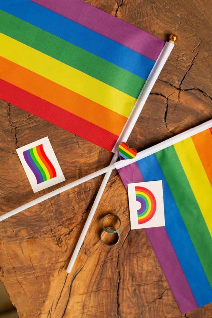 Rainbow pride flags and symbols arranged on a rustic wooden table, representing LGBTQ+ pride and unity.
